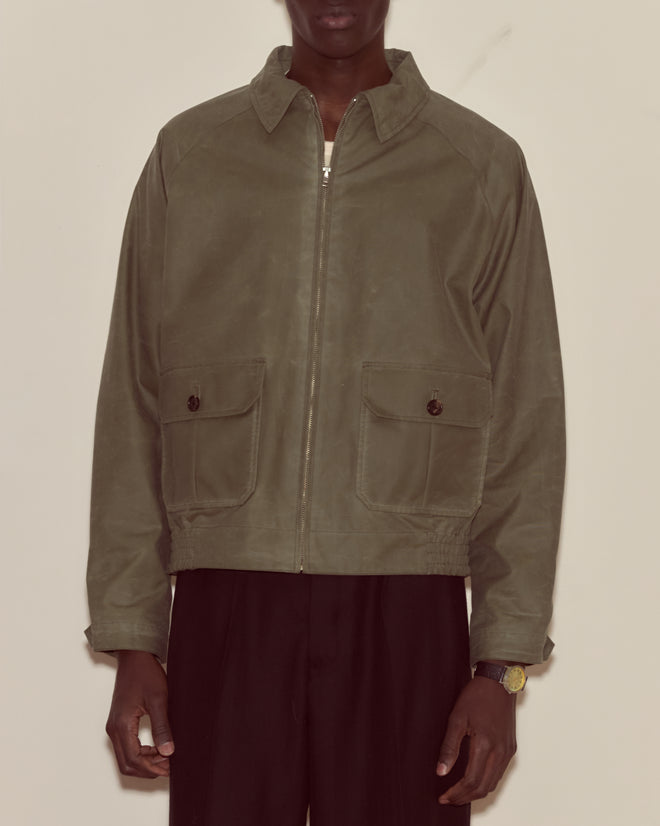 A person wearing a Waxed Coach's Jacket in light green and black pants.