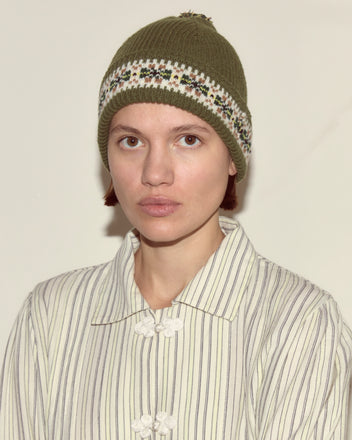 Person wearing a green Moritz Hat made of merino wool in a Fair Isle pattern and a striped buttoned shirt, looking at the camera with a neutral expression.