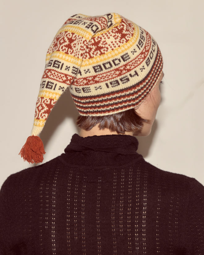 Person pictured from behind wearing the Marzipan Hat, a Norwegian knit hat with a tassel, made from 100% wool, and a black sweater.