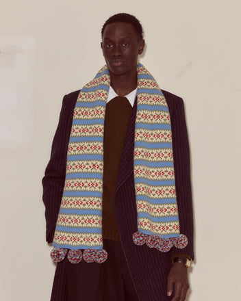 A person wearing a pinstripe coat and the Wedgewood Scarf, standing against a plain background.