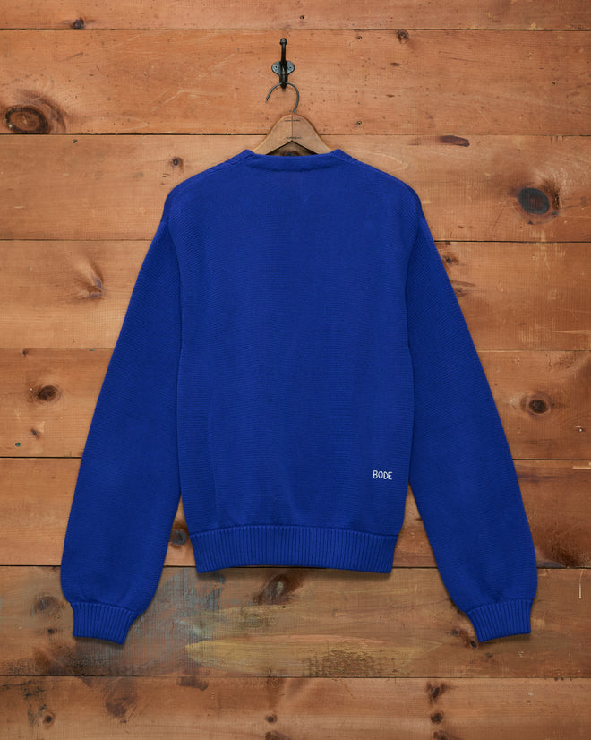 An Ultramarine Double-Breasted Cardigan hangs on a wooden wall, displayed with the back facing forward.
