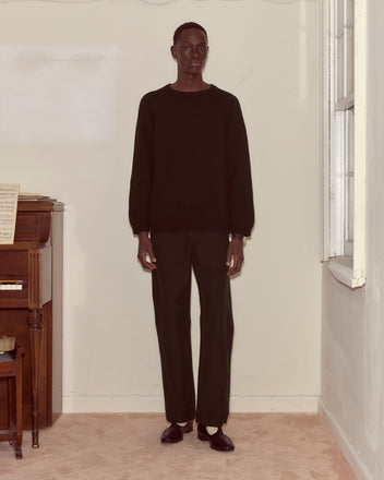 A person wearing the Cashmere Crewneck - Black with oversized pants stands indoors by a piano and window, looking at the camera.