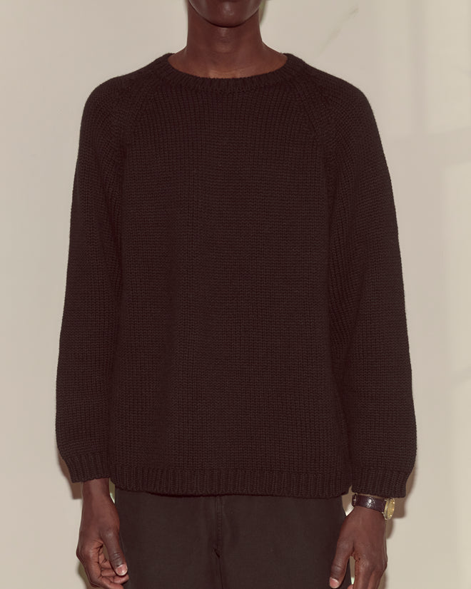 A person wearing the Cashmere Crewneck - Black with an oversized fit stands against a beige wall, arms relaxed at their sides.