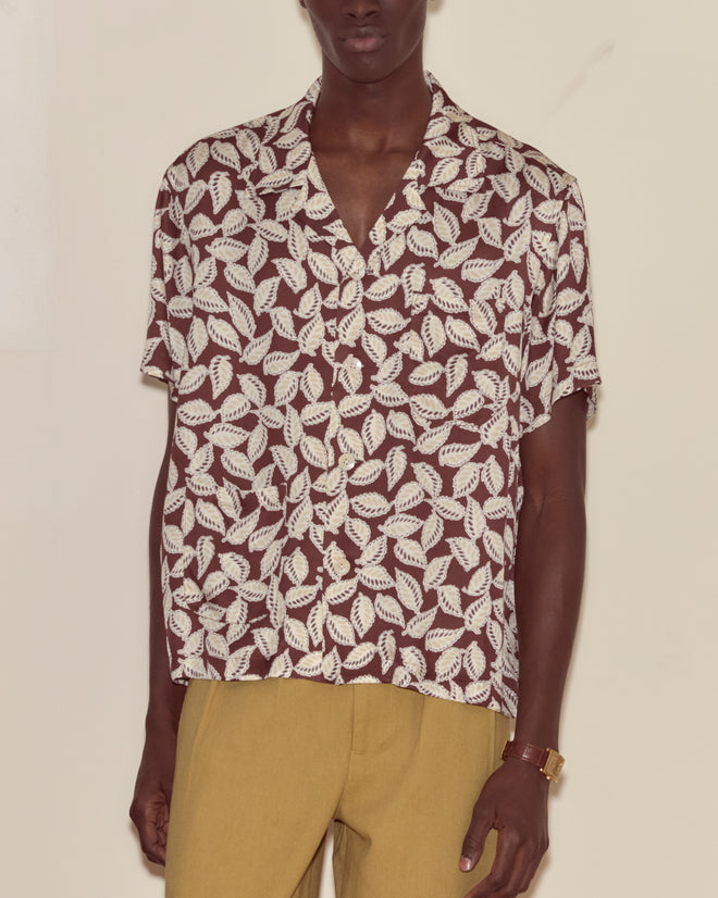 Person wearing the Paper Birch Short Sleeve Shirt, featuring a brown and white leaf-stamp pattern, paired with mustard yellow pants against a plain background.
