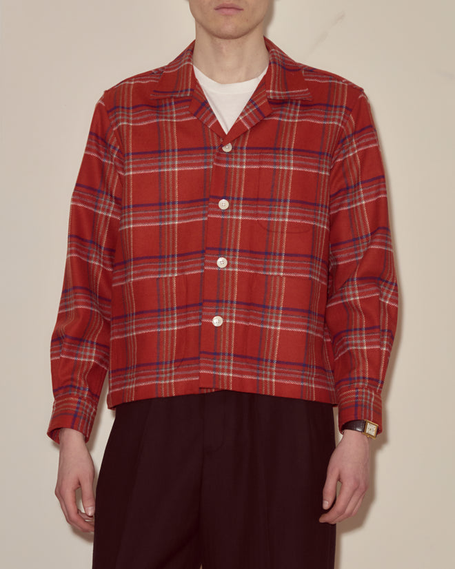 A person wears the Gable Plaid Overshirt—a red plaid flannel shirt with white buttons—paired with black trousers, standing against a plain background.