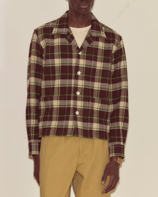 A person wearing the Woodcrest Overshirt, which features a brown and green flannel plaid pattern, paired with tan pants and a cream shirt.