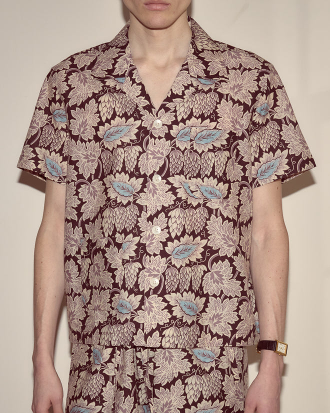 Person wearing the Wisteria Short Sleeve, a lightweight button-up shirt with matching shorts, featuring a brown and floral leaf pattern.