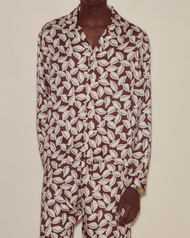 A person wearing the Paper Birch Long Sleeve Shirt, featuring a white and brown leaf-stamp pattern, paired with matching pants and standing against a plain wall.