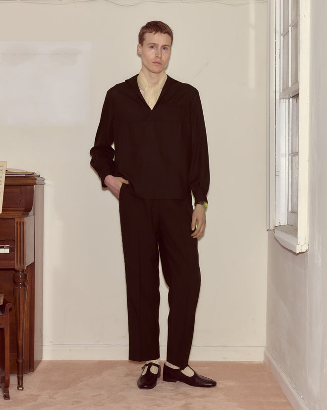 A person wearing the Shadow Cricket Shirt stands indoors by a piano and window, looking at the camera with a neutral expression.