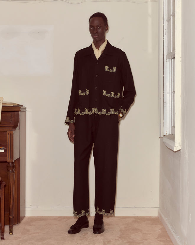 A person wearing the Laurelist Overshirt in black stands indoors near a piano and a window.