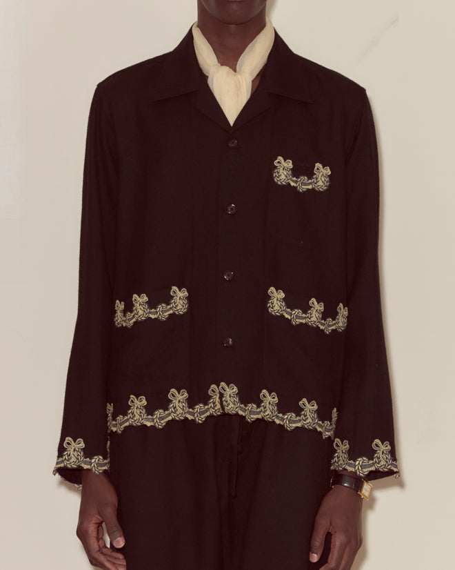 Model wearing the Laurelist Overshirt in black, featuring ornate gold embroidery and vintage passementerie, paired with a white scarf against a plain background.