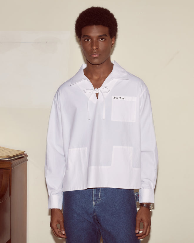A person in a Cotton Maze Long Sleeve Shirt and blue jeans stands indoors against a beige wall.