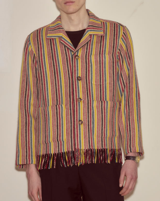 A person wearing the Lawrence Overshirt, featuring colorful vertical stripes and fringe at the hem, paired with dark pants.