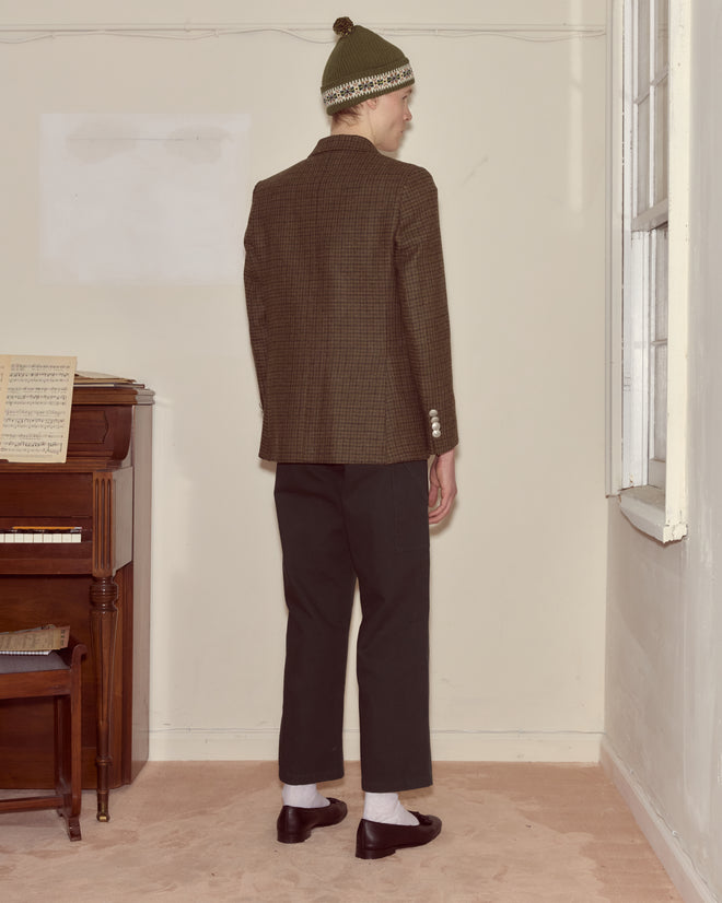 Someone wearing the Morris Houndstooth Suit Jacket in green, paired with a green beanie and black pants, stands facing away in a room with a piano.