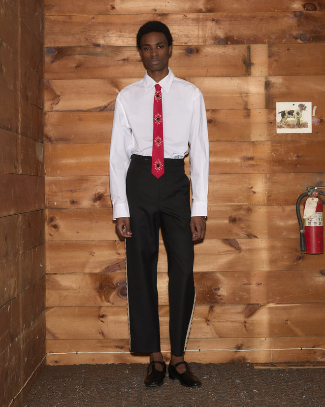 A man in a white button-down and black trousers wears a red Luminaire Tie with floral bullion embroidery.