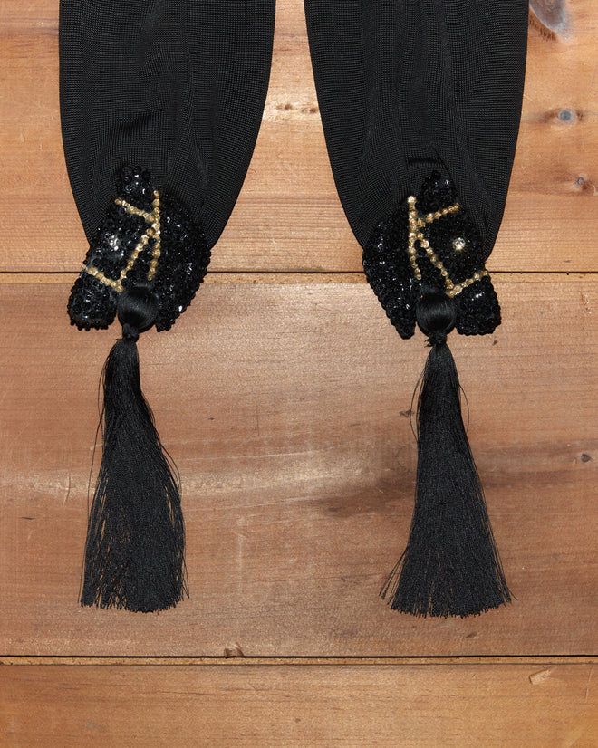 Two black Sequin Pony Scarves with beaded, sequined ends and silken tassels, reminiscent of a luxurious rayon scarf, laid on a wooden surface.