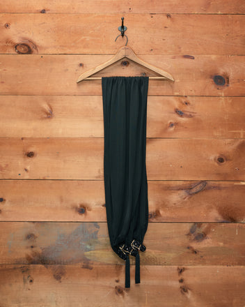 A Sequin Pony Scarf in black hangs gracefully on a wooden hanger against a rustic wooden wall.