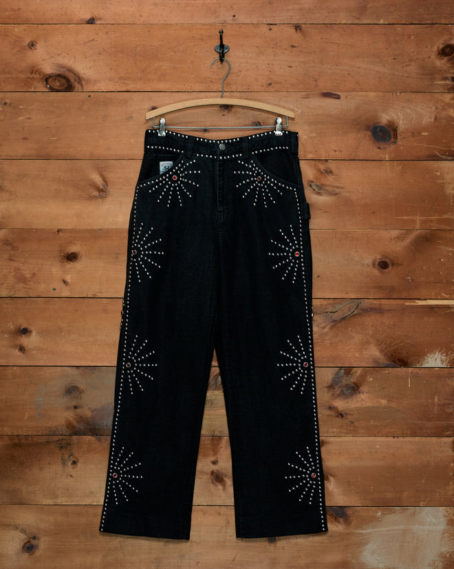 Silver Stud Knolly Brook Trousers in black cotton twill, hanging on a wooden hanger with silver stud starbursts.