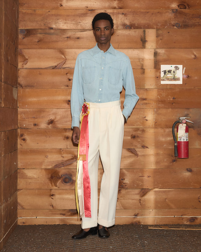 Man in a light blue button-down shirt and cream Riding Twill McNab Trousers with a decorative ribbon sash.