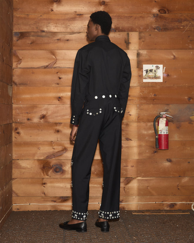 A person in a black shirt and Pearly Royal Side-Buckle Trousers with white circular side-buckles and hem details.