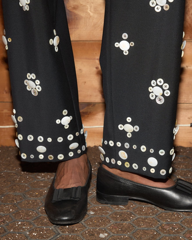 Pearly Royal Side-Buckle Trousers in black with floral pearl buttons, worn with antique-style black loafers.