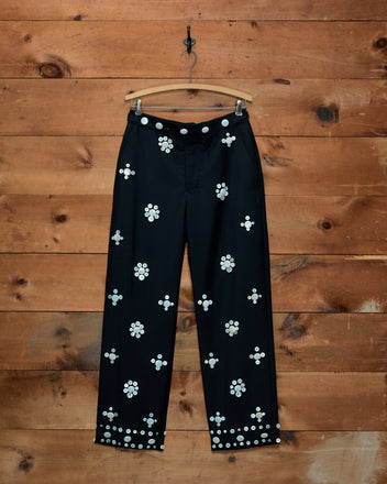 Pearly Royal Side-Buckle Trousers in black, embellished with white pearl button patterns on a wooden hanger.
