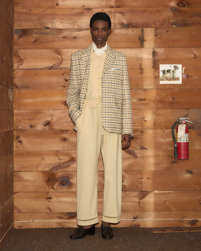 A man in a plaid blazer and cream-colored Ladder Crêpe Pajama Pants with matching ladderwork embroidery.