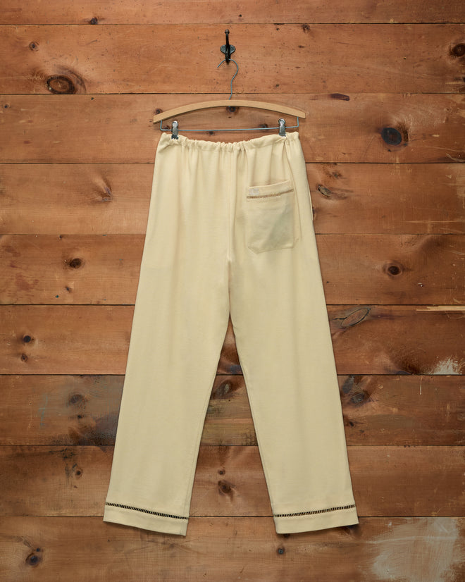 Cream-colored Ladder Crêpe Pajama Pants with a back pocket and ladderwork embroidery, hanging on a wooden hanger.