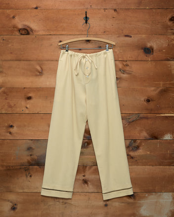 Ladder Crêpe Pajama Pants in pale yellow with ladderwork embroidery and a drawstring waist, on a wooden hanger.