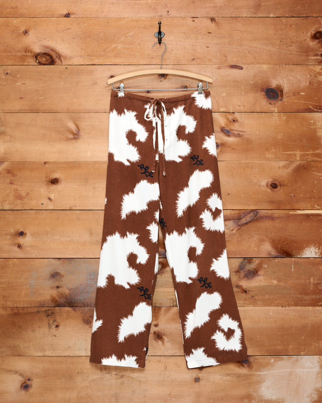 Flannel Cow Print Pajama Pants in a brown and white pattern hanging on a wooden wall.