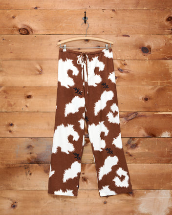 Flannel Cow Print Pajama Pants in a brown and white pattern hanging on a wooden wall.