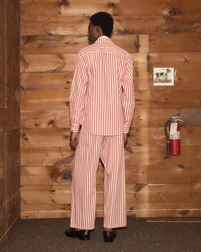 A person wearing Rancho Pajama Pants in red and white stripes stands facing a wooden wall, next to a fire extinguisher and a picture of a dog.