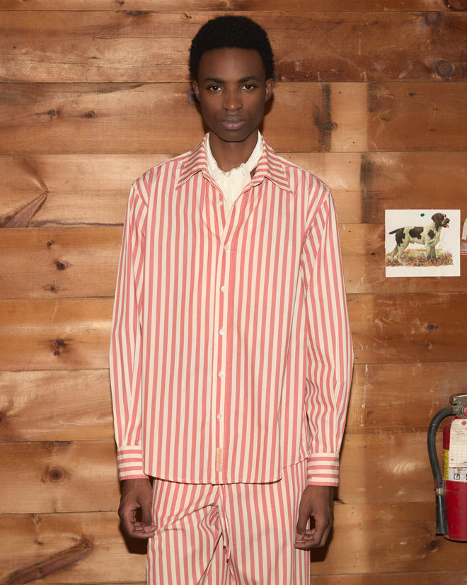 A person wearing Rancho Pajama Pants in a red and white striped pattern stands against a wooden wall adorned with a dog picture and fire extinguisher.