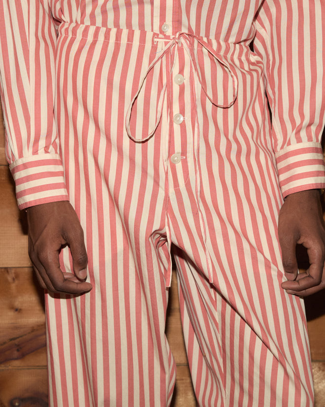 Person wearing Rancho Pajama Pants in a red and white stripe, made from 100% cotton, shown from shoulders to knees while standing in front of wood paneling.
