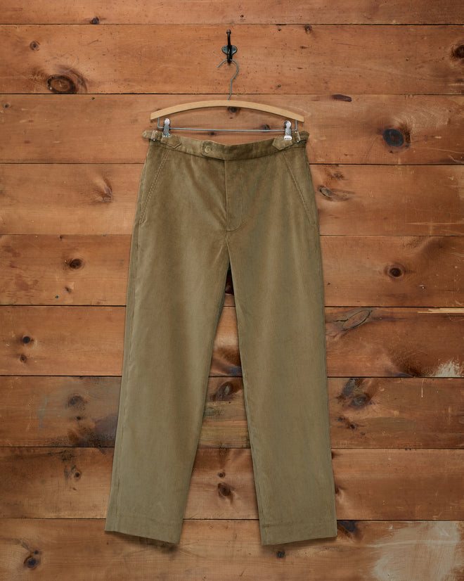 Tan Corduroy Side-Buckle Trousers hanging on a wooden hanger against a wood-paneled wall.