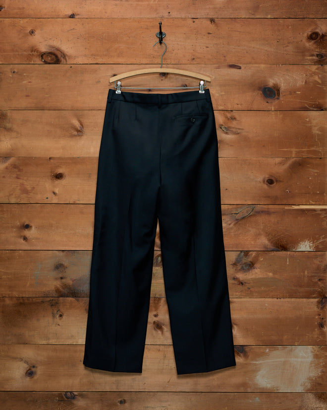 Black Mohair McNab Trousers, high-rise and wide-leg, hanging on a wooden hanger against a wood-paneled wall.