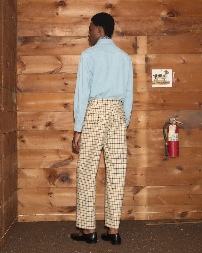 A person wearing a light blue button-up shirt and Sandhill Plaid Trousers in a classic cream-colored silhouette.