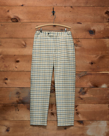 Sandhill Plaid Trousers in a cream, black, and brown checked pattern hanging on a wooden hanger.