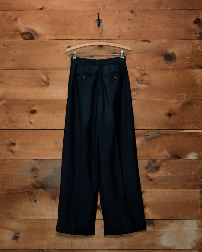 Sonora Mohair Trousers: black high-rise, wide-leg trousers with back pockets, on a hanger against a wood-paneled wall.