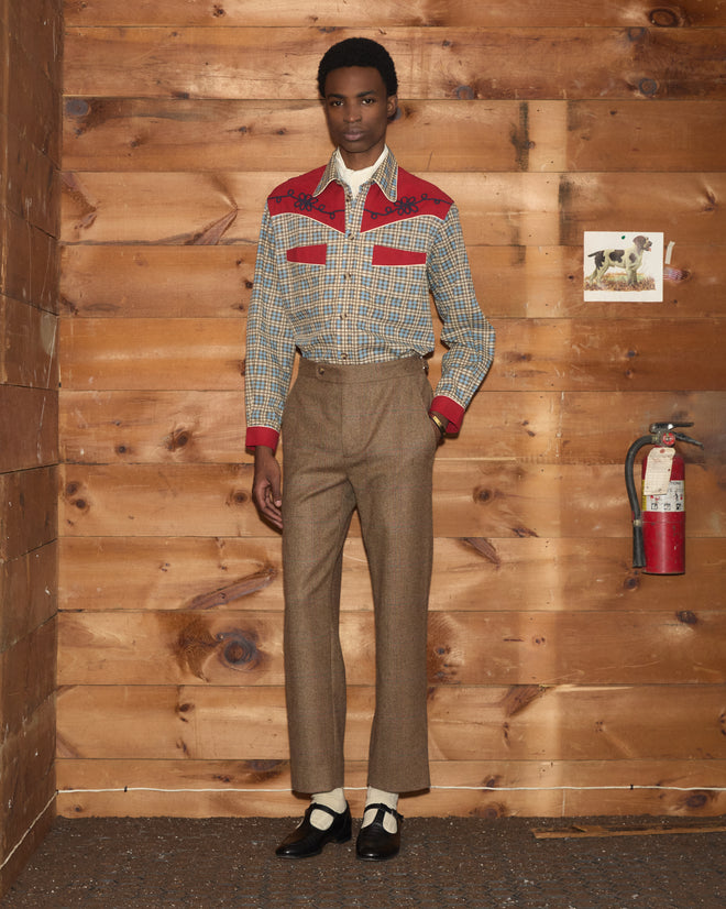 A person wearing a plaid western shirt with red yokes and brown Fremont Herringbone Trousers.