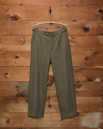 Fremont Herringbone Trousers in brown herringbone tweed with a subtle plaid pattern, hanging on a wooden hanger.