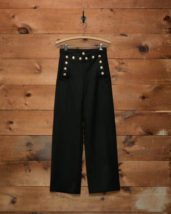 Cavalry Sailor Trousers in navy, high-waisted with double rows of gold horsehead buttons, hanging on a hanger.