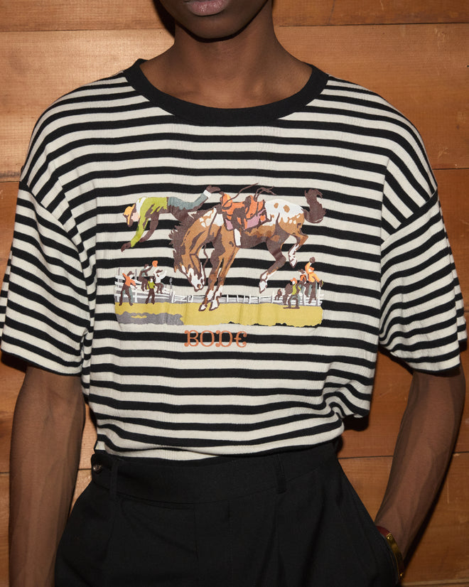Person wearing the Rib Stripe Rodeo Tee, featuring a horse and rider graphic and the word “BODE” on the front, crafted from 100% cotton.