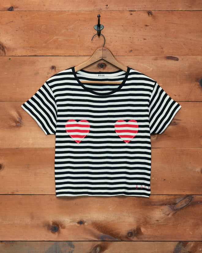 Rib Stripe Heart Tee featuring black and white stripes and two red hearts on the chest, displayed on a wooden wall.