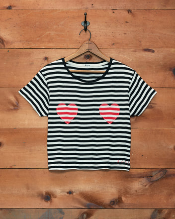 Rib Stripe Heart Tee featuring black and white stripes and two red hearts on the chest, displayed on a wooden wall.