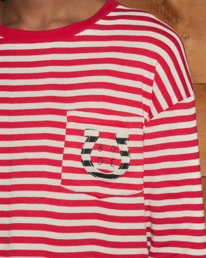 Introducing the Rib Stripe Horseshoe Long Sleeve Tee—a red and white striped top crafted from soft ribbed cotton for everyday comfort, featuring a front pocket adorned with a horseshoe design and the word “BODE.” The perfect Bode tee to highlight your casual style.