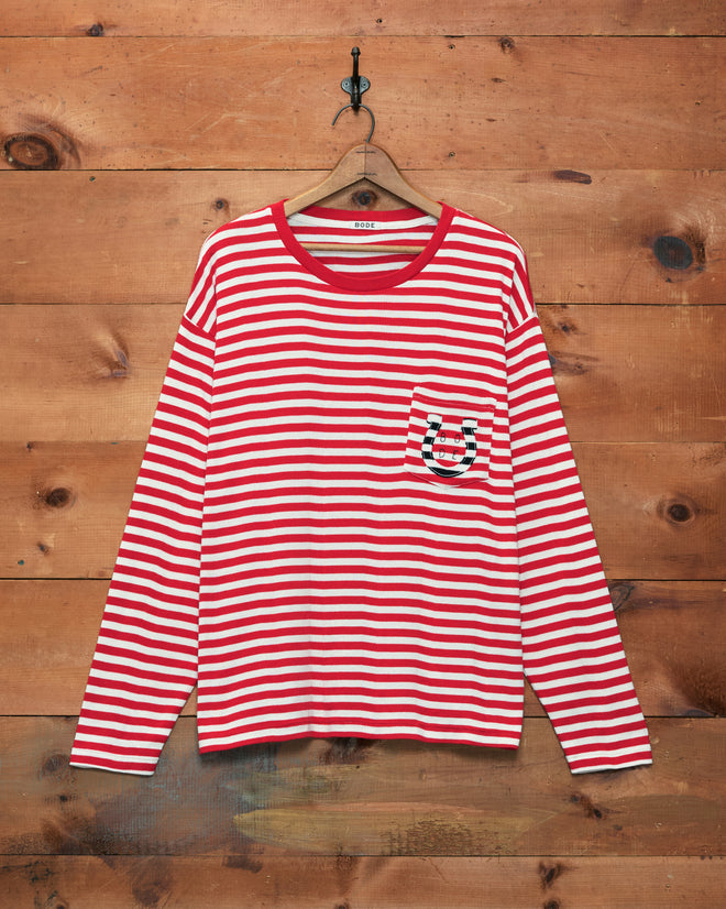 Rib Stripe Horseshoe Long Sleeve Tee, featuring red-and-white stripes, a chest pocket, and ribbed cotton fabric, displayed hanging on a wooden wall.