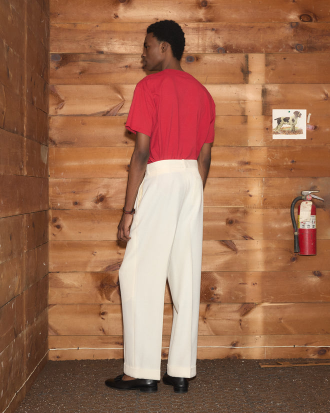 Wearing the Feed Tee and white pants, a person stands by a wooden wall featuring a fire extinguisher and a small dog photo.