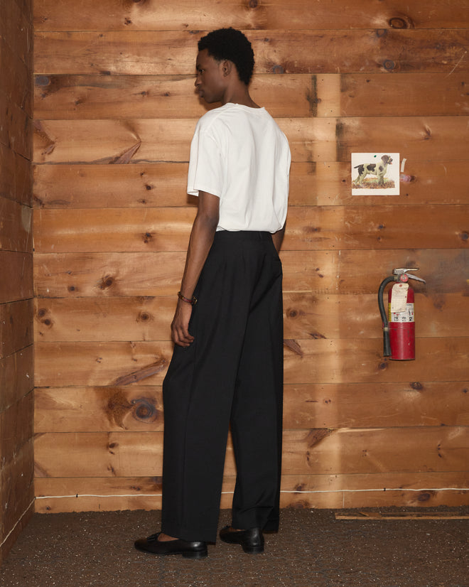 Wearing the Rodeo Bodeo Tee and black pants, a person stands sideways in a wooden room near a fire extinguisher.