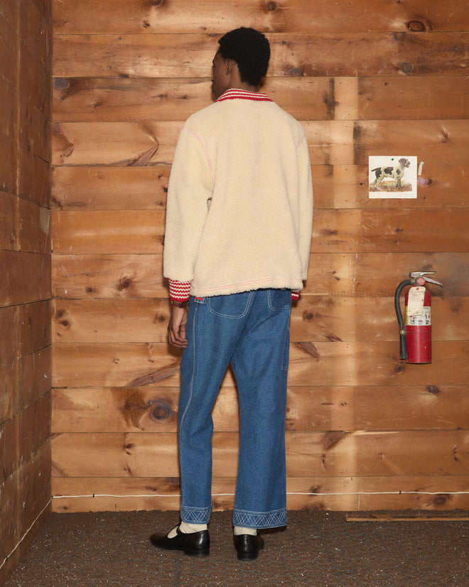 A person seen from behind wearing a cream-colored Woolly Warmup Jacket with striped cuffs and blue jeans.